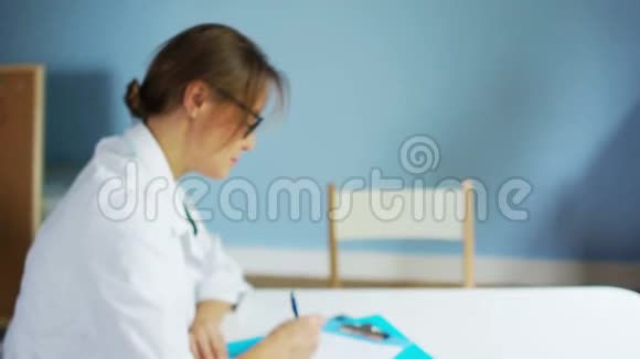 穿着白大褂戴眼镜的女医生为坐在办公桌前的病人开药方视频的预览图