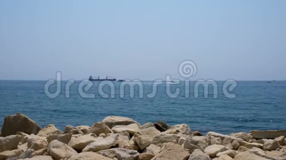 晴朗的一天开放的大海蓝天远处的船只海滩上的石头和无边无际的地平线视频的预览图