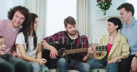 多民族的快乐和有魅力的朋友在一个大客厅里一起玩他们用吉他唱歌视频的预览图