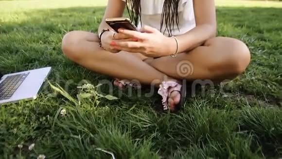 一个女孩坐在公园里写信息打电话黑发女人打电话在公园里漫游女孩打电话给她的朋友视频的预览图