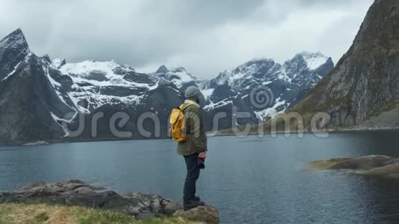 徒步旅行者欣赏雪山峰景带黄色背包的男性徒步旅行者的低角度后景享受视频的预览图