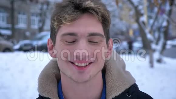 在一个大雪纷飞的冬日里年轻迷人的白种人男性看着摄像机微笑着站在外面视频的预览图