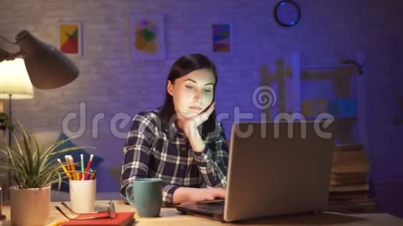 年轻女孩坐在她的现代公寓里看着笔记本电脑上令人震惊的内容视频的预览图