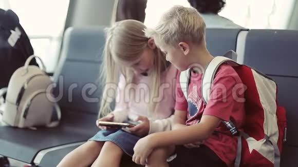 一个男孩和一个女孩坐在机场玩手机视频的预览图