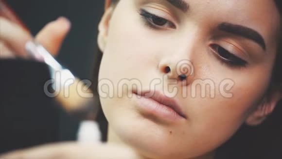 年轻漂亮的女孩靠近照镜子在脸上涂一层补品霜在一个黑色背景上视频的预览图