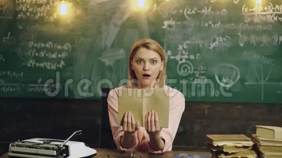 吃惊的女人在教室里用绿色黑板读一本书令人震惊的女学生拿着这本书视频的预览图