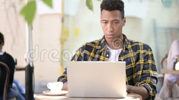 非洲年轻人喝咖啡在笔记本电脑上工作户外咖啡馆视频的预览图