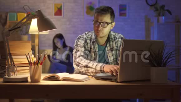 一个晚上坐在笔记本电脑前工作过度的年轻人的肖像视频的预览图