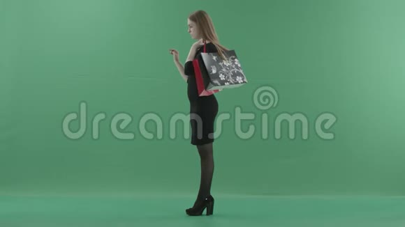 美丽的女人穿着黑色的小连衣裙手里拿着购物袋在数字屏幕上滚动她站在左边视频的预览图