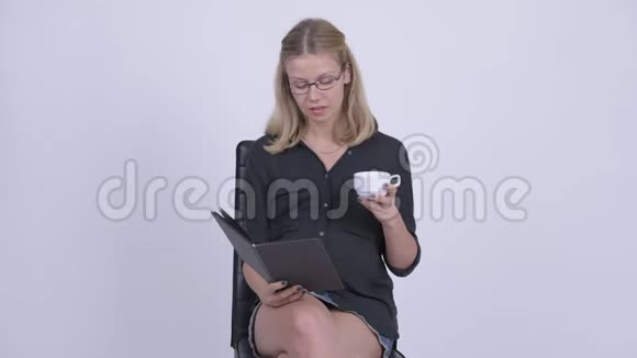 年轻快乐的怀孕女商人坐着看书喝咖啡视频的预览图