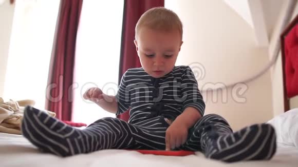 一个可爱的婴儿点击智能手机坐在大床上慢动作视频的预览图