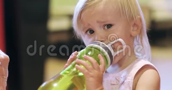 一个金发小女孩在咖啡馆里拿着一个瓶子玩视频的预览图