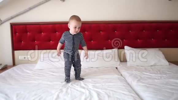 快乐的金发小男孩慢吞吞地跳上旅馆房间的大床视频的预览图