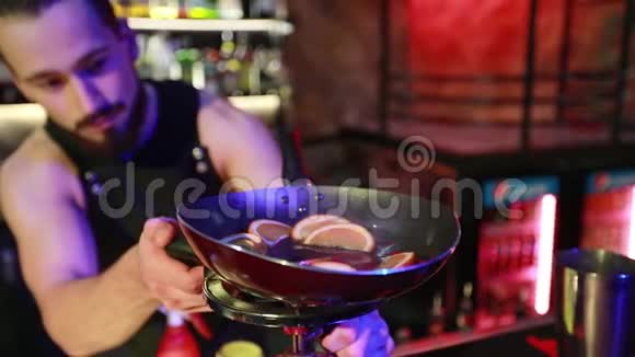 大胡子的酒吧老板在一个夜间酒吧的圆形煤气圈上准备一杯鸡尾酒视频的预览图