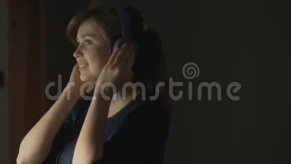 年轻女子带着耳机在家听音乐快乐的女孩跳舞把头移向歌曲的节拍站在T附近视频的预览图