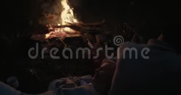 一对年轻夫妇晚上坐在火边这家伙弹吉他他的女朋友躺在他的腿上听着视频的预览图