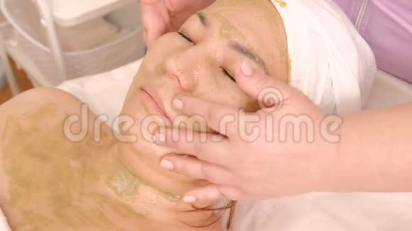面部和颈部按摩用海藻滋养面膜美容师的手抚摸着亚洲女人的皮肤再生生殖视频的预览图