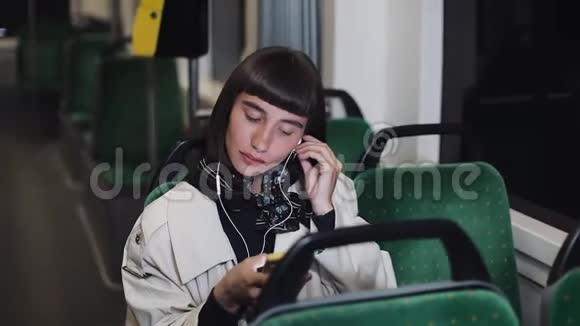 年轻时尚的女人戴着耳机在公共交通工具上听手机音乐城市灯光视频的预览图
