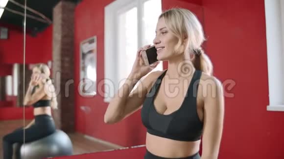 健身妇女在健身房打手机年轻女子坐着健身球视频的预览图