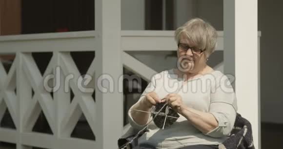 在红镜头下拍摄的Terrasse房子的门廊上一位年长的女人在户外打着针织坐着微笑视频的预览图