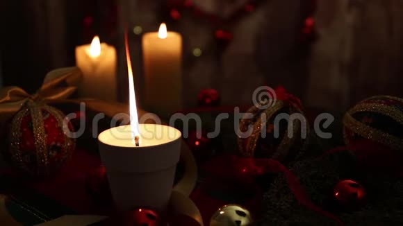 圣诞节的气氛三支点燃的蜡烛一支在前景上有大火焰的蜡烛红色和金色的脱钩的球缎子的金丝带视频的预览图