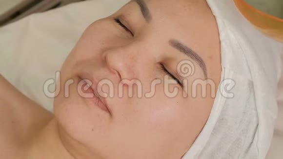 一位专业的美容师在一位亚洲女性的脸上涂上海藻酸钠面具特写镜头黄鹂的复壮程序视频的预览图