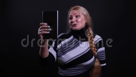 在平板电脑上播放视频的中年白种人女性特写镜头背景与黑色隔离视频的预览图