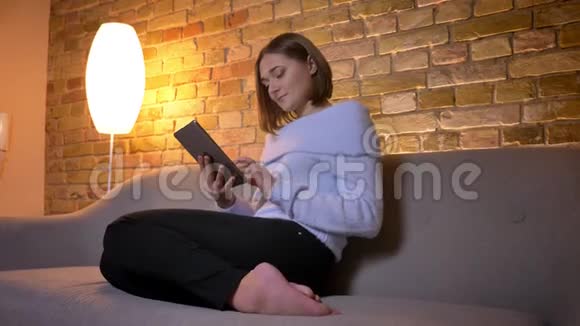 年轻漂亮的白人女性轻敲平板电脑然后转向镜头微笑着坐在视频的预览图