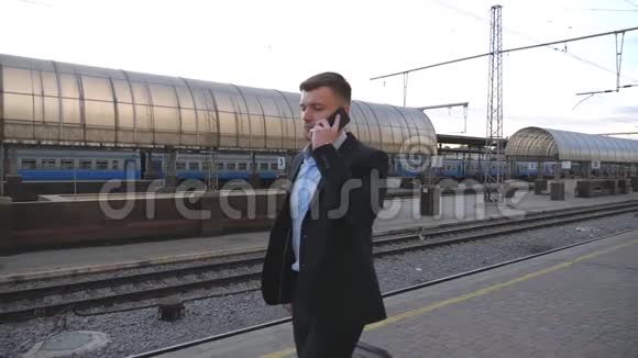 英俊的商人带着行李穿过火车站打电话青年商业人士视频的预览图