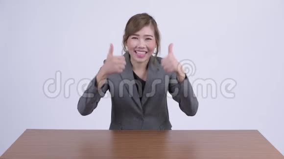 年轻快乐的亚洲女商人一边竖起大拇指一边兴奋地看着桌子视频的预览图