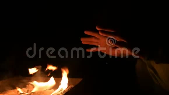 一个人在完全的黑暗中把手放在明火上取暖男人夜晚的炉火旁视频的预览图