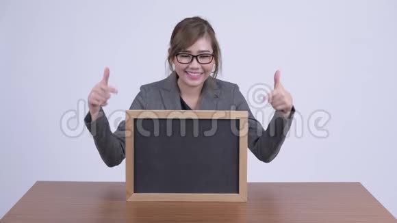 年轻快乐的亚洲女商人在办公桌前展示黑板竖起大拇指视频的预览图