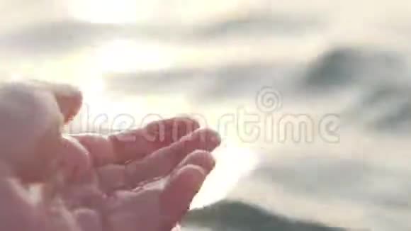 雄性的手在日落时的阳光下玩得很开心轻轻地接触海面特写视频的预览图