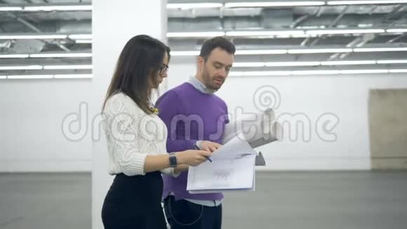 一个女人和一个男人正拿着建筑图纸沿着大厅走视频的预览图