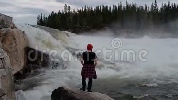 清晨旅行者站在挪威森林瀑布前穿着红帽子视频的预览图