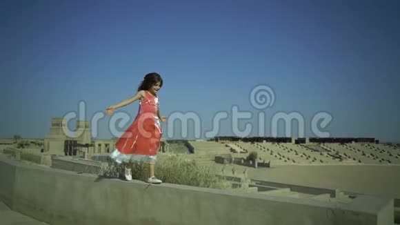 小可爱的女孩走在墙上的大圆形剧场孩子有一个梦想孩子从栅栏上跳下来粉红色的裙子飘进来视频的预览图