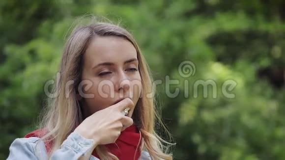 年轻的女人用喉咙喷雾站在公园的背景上健康和医疗理念视频的预览图