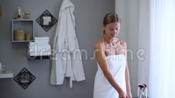 淋浴后用毛巾裹着美丽的女人用玉辊按摩脸部视频的预览图