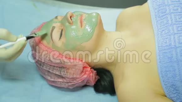 戴手套的美容师给一个女人戴上用刷子做的灰色粘土做的化妆面具侧视图视频的预览图