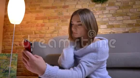 一张年轻漂亮的白种人女性在电话中自拍的特写照片她一个舒适的室内公寓里视频的预览图
