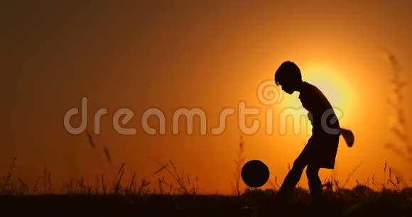 一个男孩在海滩上踢足球或踢足球的剪影背景是美丽的日落视频的预览图
