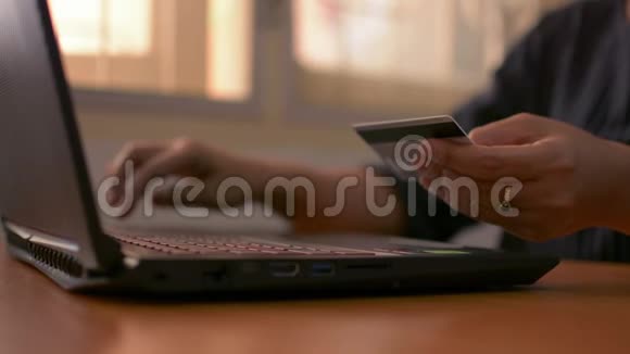 一个女人的手拿着一张信用卡在桌子上键入笔记本电脑键盘进行在线支付视频的预览图