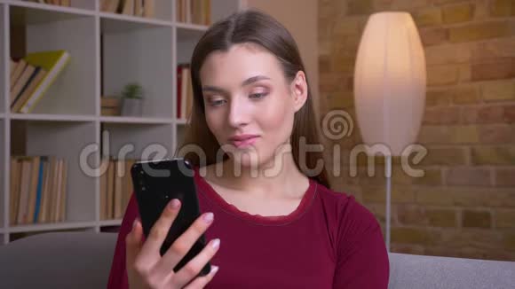 年轻快乐的黑发女性展示直立的绿色手机屏幕推荐应用在家里视频的预览图