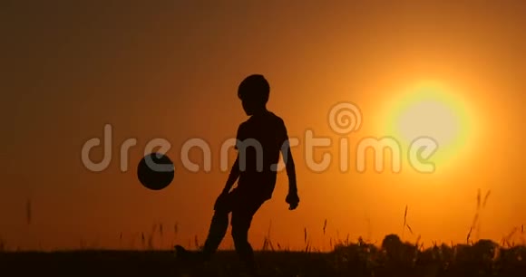 一个男孩在海滩上踢足球或踢足球的剪影背景是美丽的日落视频的预览图