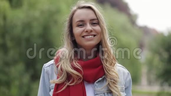 年轻漂亮的女人笑着快乐地享受着积极的生活方式戴着红领巾站在公园里关闭视频的预览图