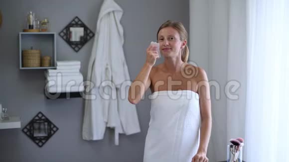 淋浴后用毛巾裹着美丽的女人用玉石按摩按摩脸部视频的预览图