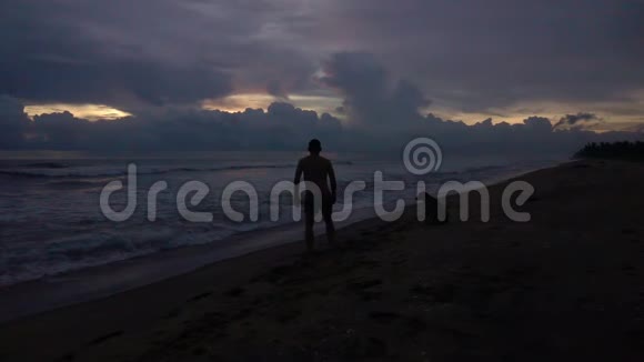 日落时分快乐的年轻男性剪影在海滩上跳跃举起双手视频的预览图
