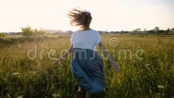 穿着一件连衣裙的女人浪漫地跑过田野夕阳下有高高的草地动作缓慢镜头移动视频的预览图