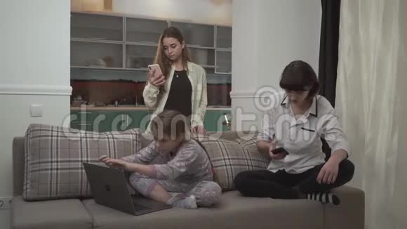 两个姐姐在手机上发短信小女孩坐在家里的沙发上用笔记本电脑打字小可爱视频的预览图