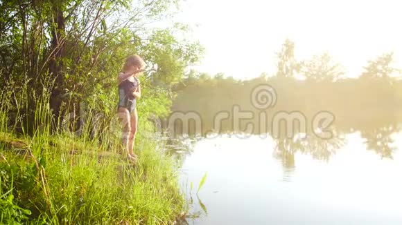 小女孩用棍子在河里钓鱼美丽的日落扩散的光芒视频的预览图